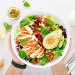 Grilled chicken meat and fresh vegetable salad of tomato, avocado, lettuce and spinach. Healthy and detox food concept. Ketogenic diet. Buddha bowl in hands on white background, top view